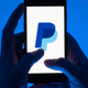 A woman holds a smartphone with the logo of the payment service Paypal.